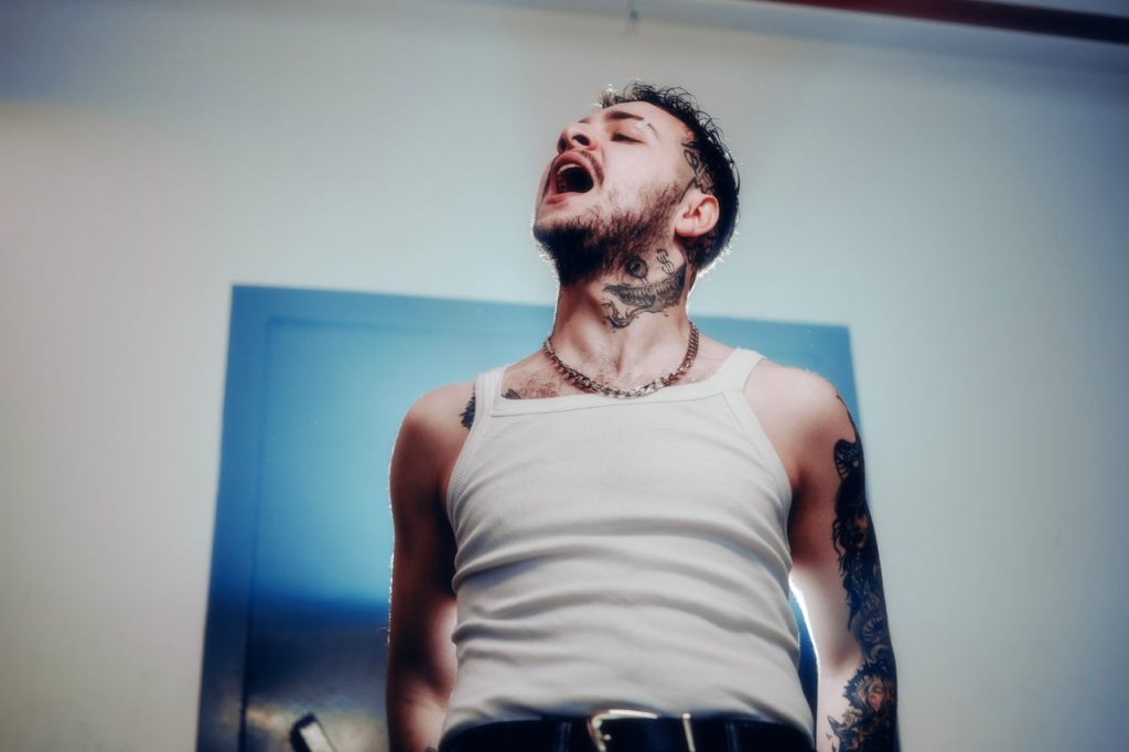 A dynamic portrait of a tattooed man in a white tank top, exuding emotion and style.