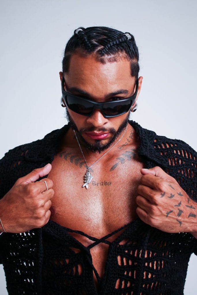 Confident man in sunglasses and tattoos posing with open shirt.